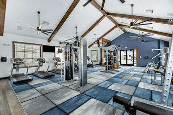 A gym with weights and cardio equipment and ceiling fans